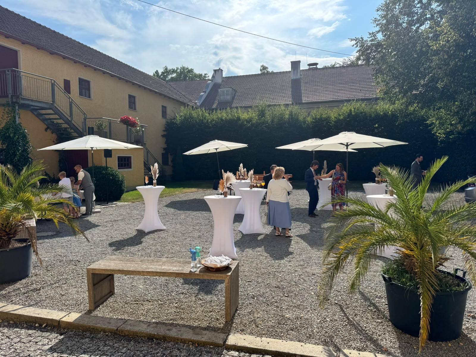 Sommerlicher Sektempfang mit Stehtischen und Palmen im Innenhof des Gut Schwabhof