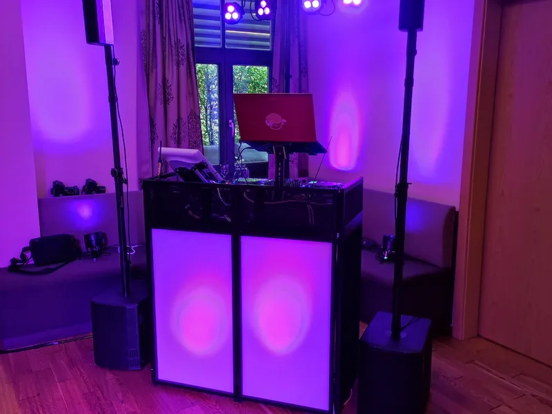 DJ-Setup von der Seite mit pinkfarbenem Raumlicht und Lichtstativen – Hochzeits DJ Rico Cinsano